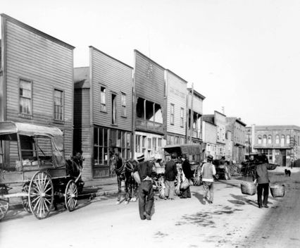 1907 年華埠 Dupont Street（現 Pender Street）一景。圖右負担挑的行人上方即為被裁之前的 Sam Kee Building 外貌。（City of Vancouver Archives 1376-506）